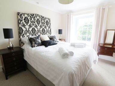 A bedroom with a bed with patterned headboard pillows and rolled towels bedside tables with lamps and a window at Dolau Farmhouse in Lampeter