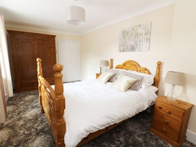 A bedroom with a wooden bed and nightstand and a wooden wardrobe at Dolau Farmhouse in Lampeter