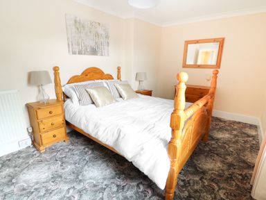 A bedroom with a wooden bed and bedside tables with lamps a dresser with a mirror and a painting on the wall at Dolau Farmhouse in Lampeter