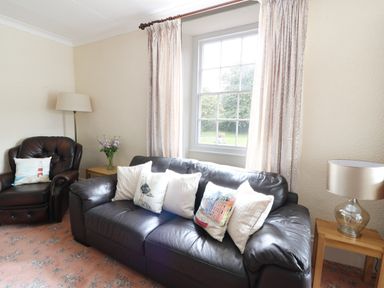 A living room with a black leather sofa and armchair with cushions beside a window at Dolau Farmhouse in Lampeter