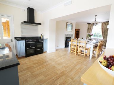 A kitchen with black stove and light blue cabinets next to a dining area with a white table and wooden chairs at Dolau Farmhouse in Lampeter
