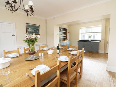 A dining room with a wooden table set for eight with white dishes and a vase of flowers at Dolau Farmhouse in Lampeter