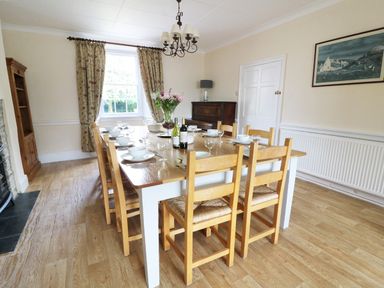 A dining room with a wooden table set with white dishes and wine bottles surrounded by wooden chairs at Dolau Farmhouse in Lampeter