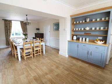 A dining room with a wooden table set for food and a blue cabinet with cups and a fruit bowl at Dolau Farmhouse Lampeter