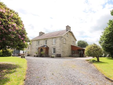 A stone farmhouse with a gravel driveway and trees nearby at Dolau Farmhouse in Lampeter