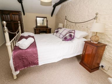 A bedroom with a bed featuring white and purple bedding a wooden bedside table with a lamp wooden dresser with a mirror and a wardrobe at Dolau Farmhouse in Lampeter