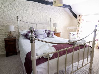 A bedroom with a metal bed frame two bedside tables with lamps and a rocking chair at Dolau Farmhouse in Lampeter
