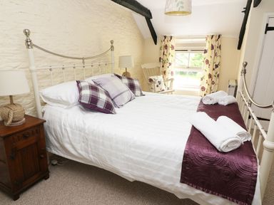 A bedroom with a metal bed frame white bedding and purple cushions at Dolau Farmhouse in Lampeter