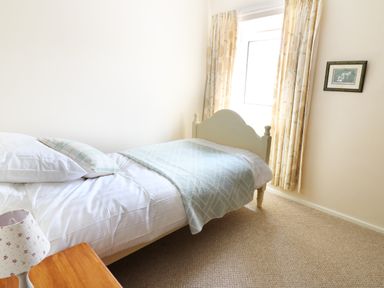 A bedroom with a single bed a side table with a lamp curtains on the window and a framed picture on the wall at Dolau Farmhouse in Lampeter
