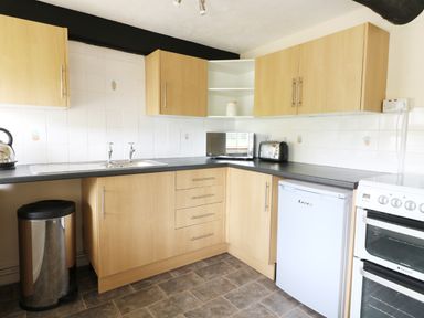 A kitchen with wooden cabinets a black countertop a microwave toaster small fridge and stove at Dolau Farmhouse in Lampeter