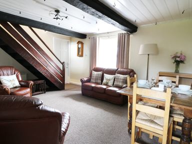 A living room with leather sofas wooden dining table chairs and a staircase at Dolau Farmhouse in Lampeter