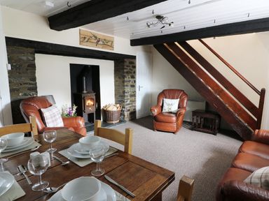 A living room with a dining table set for four a wood burning stove and leather armchairs at Dolau Farmhouse in Lampeter