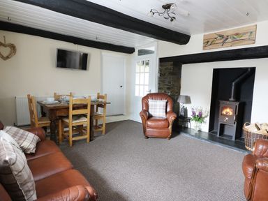 A living room with leather chairs a wooden dining table a wall-mounted TV and a wood-burning stove at Dolau Farmhouse in Lampeter