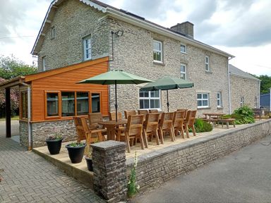 An outdoor patio with wooden tables and chairs under green umbrellas beside a stone building at Dolau Farmhouse in Lampeter