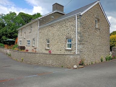 A stone farmhouse with multiple windows and patio furniture on a paved area at Dolau Farmhouse in Lampeter