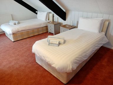 A bedroom with two single beds bedside tables and rolled towels on each bed at Dolau Farmhouse in Lampeter