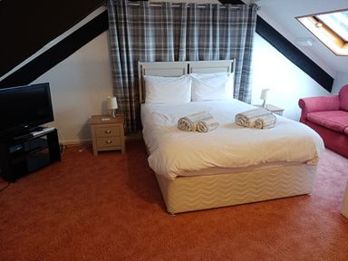 A bedroom with a double bed towels on the bed nightstands with lamps a red sofa a television and a skylight at Dolau Farmhouse in Lampeter