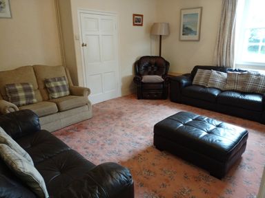 A living room with sofas armchair ottoman floor lamp and window at Dolau Farmhouse in Lampeter
