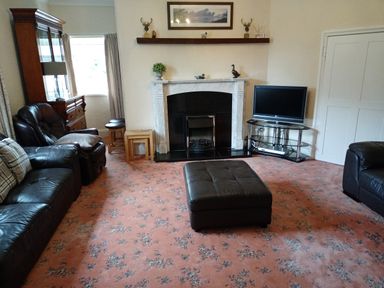 A living room with leather sofas a fireplace and a television on a stand at Dolau Farmhouse in Lampeter