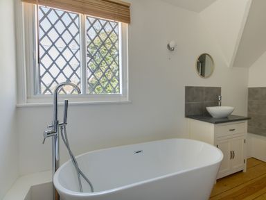A bathroom with a freestanding bathtub a sink on a cabinet and a window with lattice design at The Old School House in Piddletrenthide