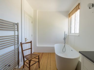 A bathroom with a freestanding bathtub a wooden chair a window with blinds and a heated towel rail at The Old School House in Piddletrenthide