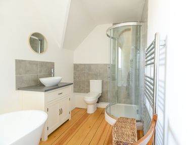 A bathroom with a shower enclosure a toilet a sink vanity a round mirror a towel rack and a wicker basket at The Old School House in Piddletrenthide