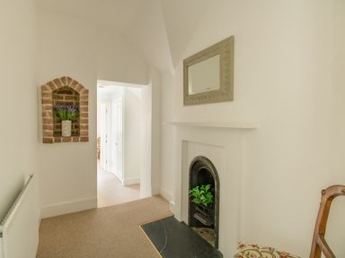 A hallway with a small decorative fireplace a mirror above and a brick wall niche with flowers at The Old School House in Piddletrenthide