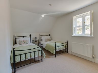A bedroom with two single beds with green blankets and a small side table with a lamp at The Old School House in Piddletrenthide