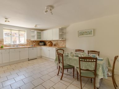 A kitchen with white cabinets a dining table with chairs and a picture on the wall at The Old School House in Piddletrenthide