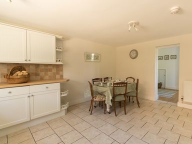 A kitchen with white cabinets a basket on the counter a dining table with a tablecloth and four chairs at The Old School House in Piddletrenthide