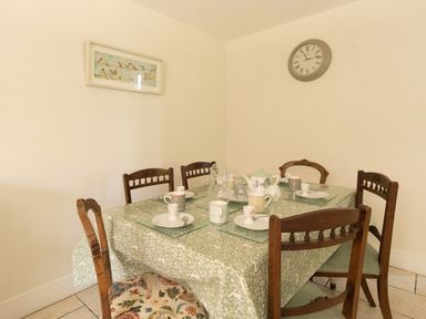 A dining room with a table set for tea with six wooden chairs at The Old School House in Piddletrenthide