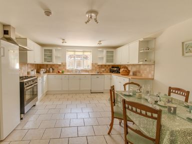 A kitchen with tiled floor white cabinets a dining table with chairs and tableware at The Old School House in Piddletrenthide