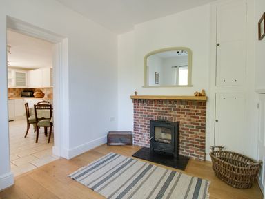 A room with a brick fireplace and wood-burning stove next to a basket and a striped rug at The Old School House in Piddletrenthide