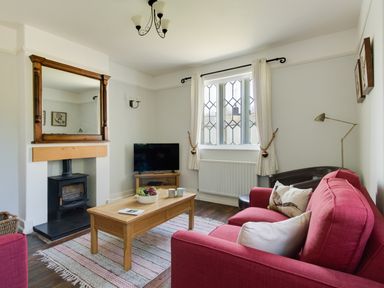 A living room with a red sofa a wooden coffee table a fireplace a television and a window with white curtains at The Old School House in Piddletrenthide