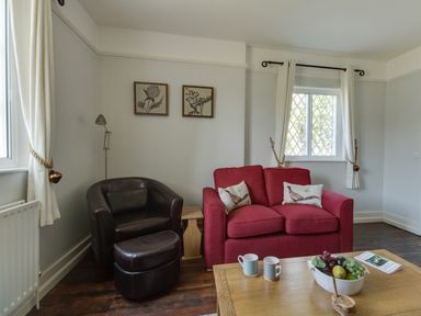 A living room with a red sofa and a brown leather armchair near windows at The Old School House in Piddletrenthide
