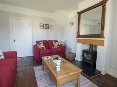A living room with red sofas a wooden coffee table a fireplace and a large mirror at The Old School House in Piddletrenthide