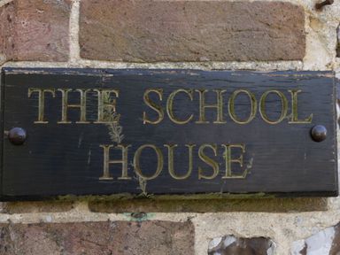 A wooden sign with the words The School House on a brick wall at The Old School House in Piddletrenthide