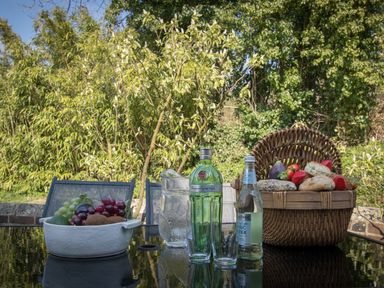 An outdoor table with a bowl of fruit a basket of bread and bottles of beverages at The Old School House in Piddletrenthide
