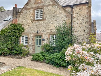 Front view of a stone and brick house with a green door surrounded by plants and flowers at The Old School House in Piddletrenthide