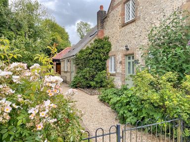 A gravel pathway leading to a green door on a stone house with plants and flowers on both sides