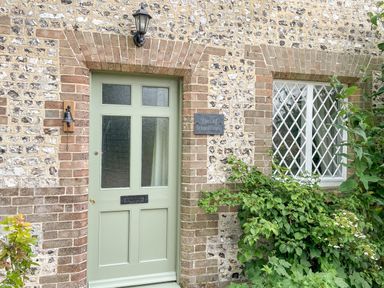An exterior wall with a green door next to a window with lattice panes and a plaque that says The Old School House in Piddletrenthide