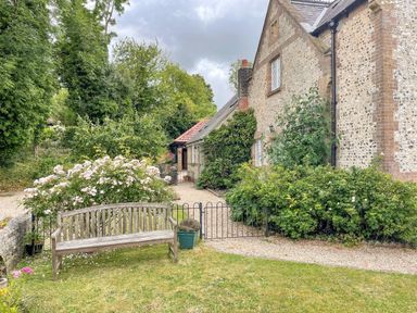 A garden bench with flowering bushes and a stone house with a gravel path at The Old School House in Piddletrenthide