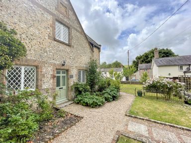 A stone house with a green door and windows with diamond panes surrounded by a garden and gravel path at The Old School House in Piddletrenthide