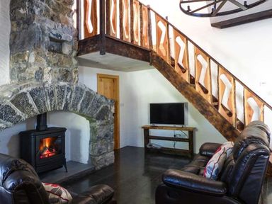 A living room with a stone fireplace wooden staircase leather sofas and a television at The Well House in Kinvara County Galway