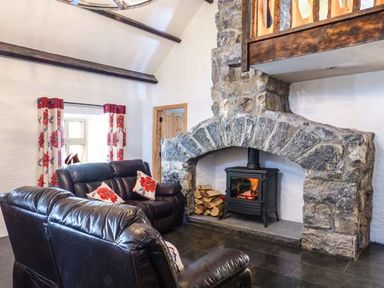 A living room with leather sofas a stone fireplace and floral curtains at The Well House in Kinvara County Galway