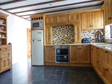 A kitchen with wooden cabinets tiled backsplash oven refrigerator microwave toaster and wine rack at The Well House in Kinvara County Galway