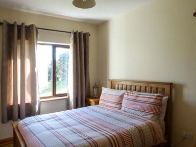 A bedroom with a wooden bed and striped bedding next to a window with brown curtains at The Well House in Kinvara County Galway