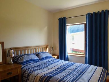 A bedroom with a wooden bed and bedside tables with lamps next to a window with blue curtains at The Well House in Kinvara County Galway