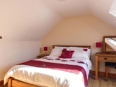 A bedroom with a wooden bed with white and red bedding two bedside tables with red lamps and a wooden dressing table with a mirror at The Well House in Kinvara County Galway