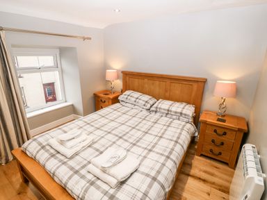 A bedroom with a wooden double bed with plaid bedding two bedside tables with lamps and a window at Haddef in Nefyn